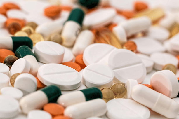 Assorted pills, tablets, and capsules in various colors, including white, orange, green, and beige.