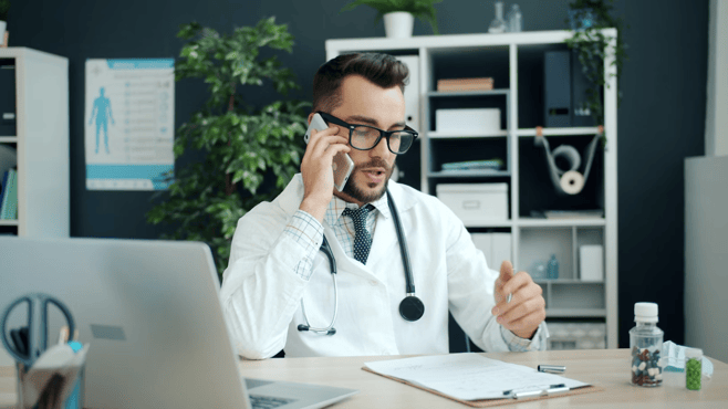 A healthcare professional in a white coat with a stethoscope writes on a clipboard