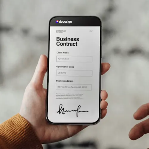 Hand holding a smartphone displaying a DocuSign mobile interface showing a Business Contract document.
