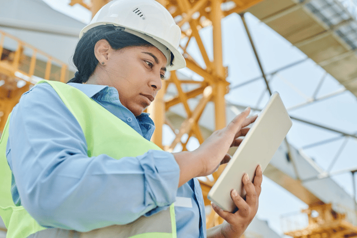 Female construction worker in hard hat and safety vest using tablet to perform a building inspection